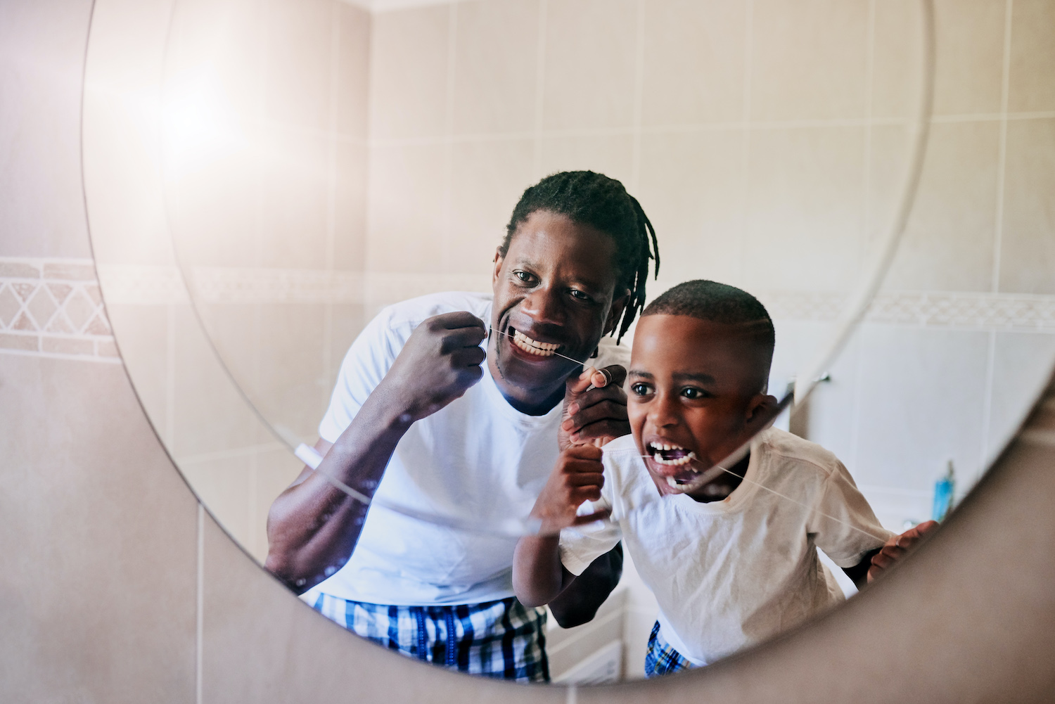 Dad and his son floss together while looking in the bathroom mirror
