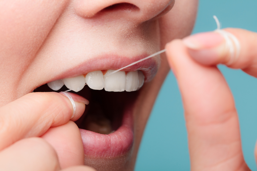 closeup of a woman flossing her teeth with string floss to keep her teeth and gums healthy