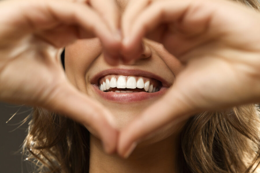 Closeup of a woman smiling behind her hands held in a heart shape