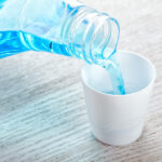 Closeup of blue mouthwash being poured into a white cup from a clear container