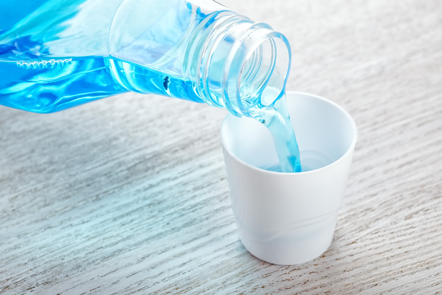 Closeup of blue mouthwash being poured into a white cup from a clear container, dentist in bentonville