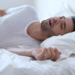 Brunette man with sleep apnea snores with his mouth open in his bed